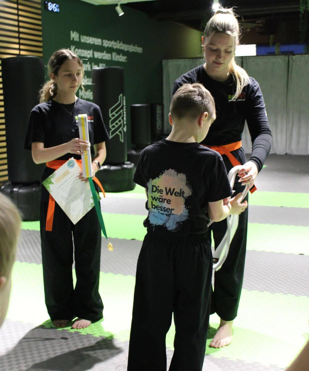 Gürtelverleihung — Kind erhält neuen Gürtel von den Coaches